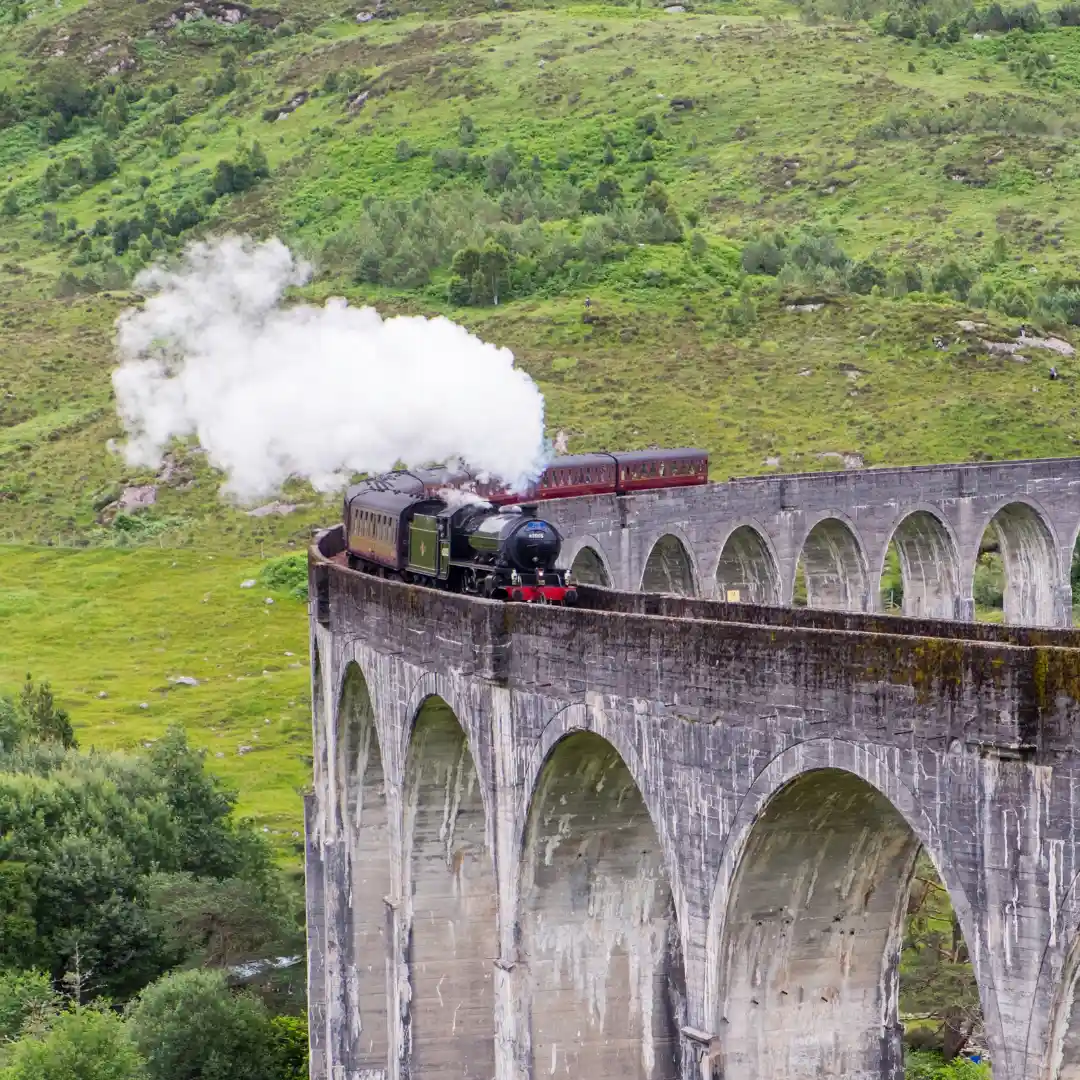 in un alto viadotto (Glenfinnan Viaduct in Scozia) un treno a vapore rosso passa lasciando fumo